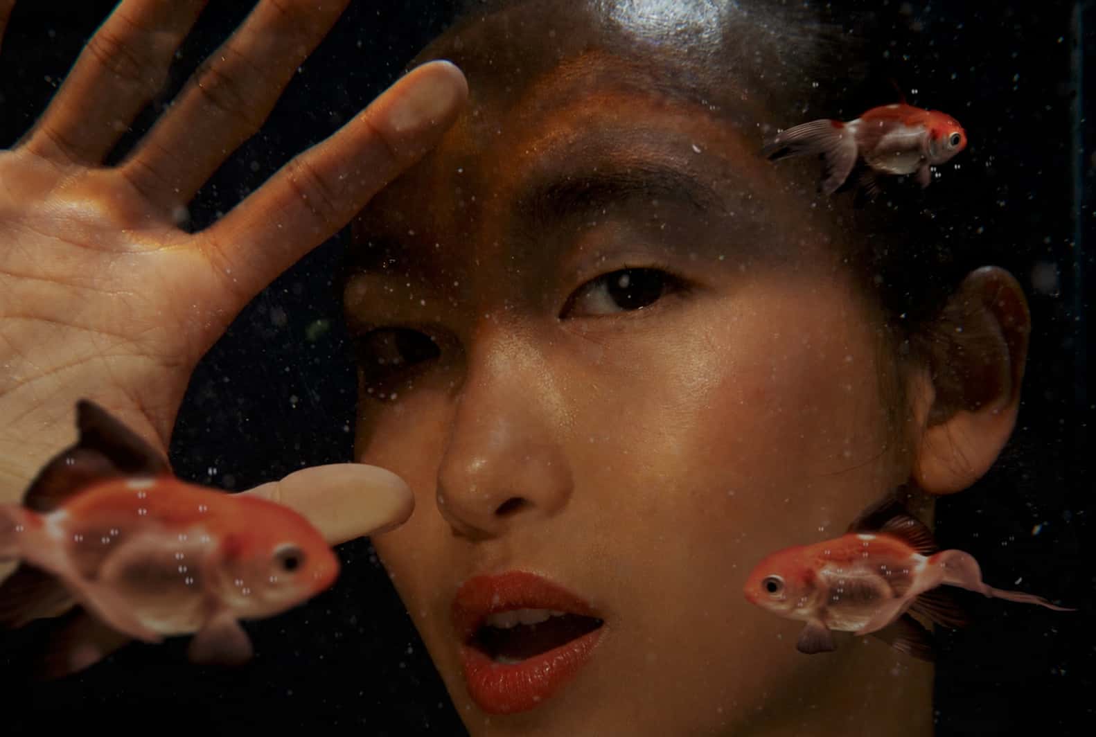 A close-up of a woman behind aquarium glass with fish in front of her